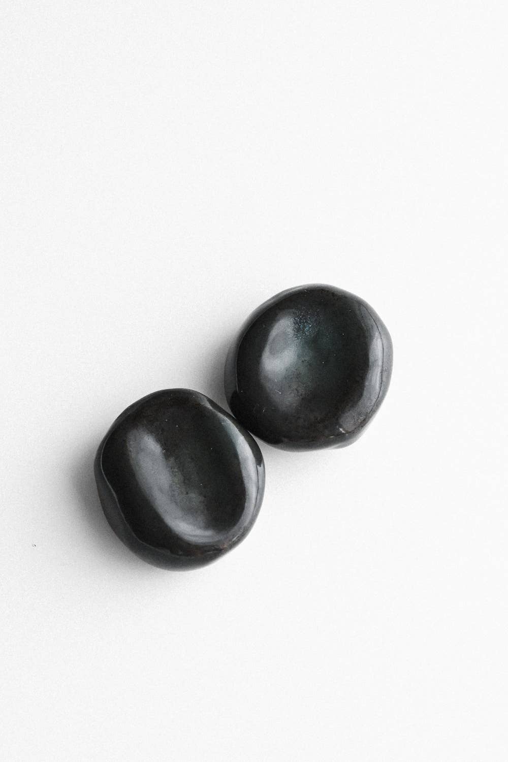 Zwei schwarze Sorgensteine mit glänzender Glasur und runden Vertiefungen.