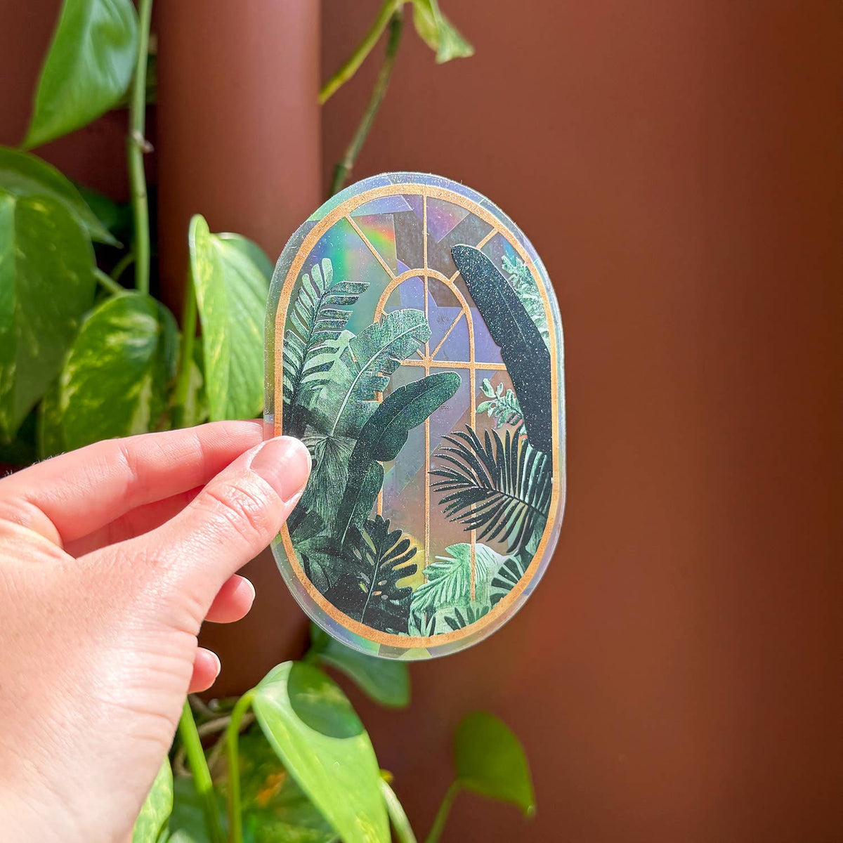 Botanischer Fenstersticker mit Blättermotiv und bogenförmigem Rahmen, in einer Hand gehalten.