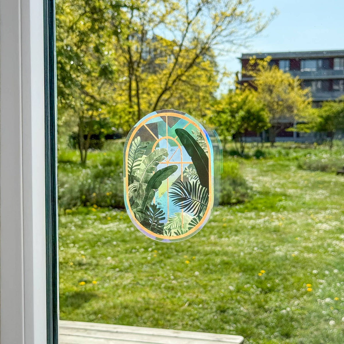 Botanischer Fenstersticker auf einer Fensterscheibe mit Blick auf eine grüne Wiese.